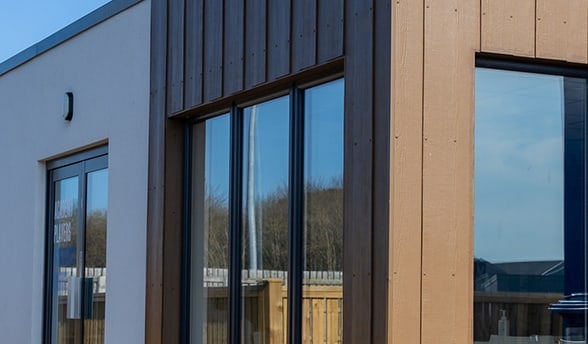 Corner of the Huddersfield Town modular building showing timber-effect cladding, dark window frames and decking