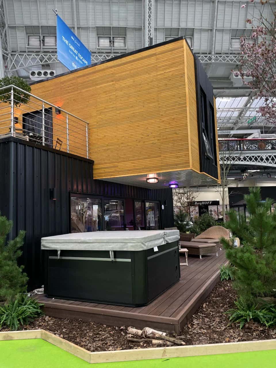 Timber-clad upper storey cantilevering over the dark ground floor of the exhibition build, with wall lights beneath