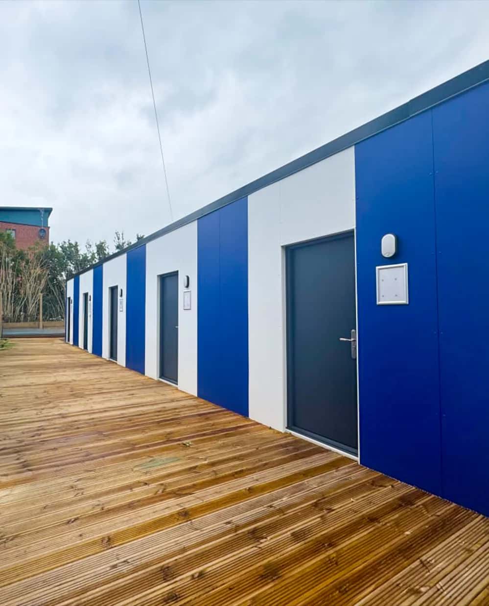Completed Sheffield Wednesday academy changing facility: white and blue panelled elevation with entrance doors along a timber-decked walkway